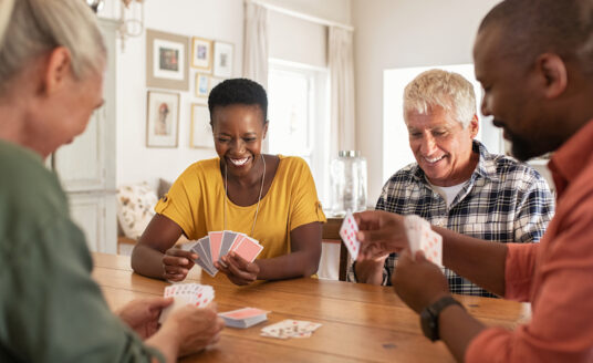 A group of seniors gather around a table to play cards indoors, an example of safe summer activities for seniors.
