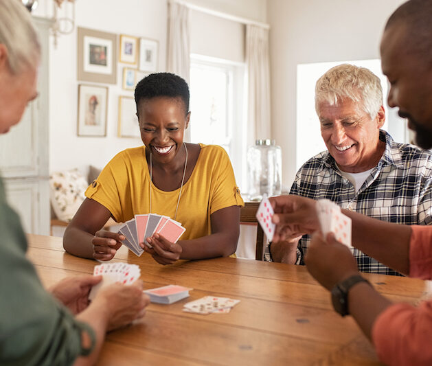 A group of seniors gather around a table to play cards indoors, an example of safe summer activities for seniors.