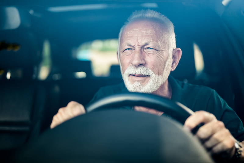 A senior aged man squints his eyes behind the wheel of a car, indicating that his vision may be impacted and it could be time to stop driving.