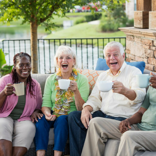 A group of happy elder men and women sitting on a couch in the outdoors having a drink in a cup