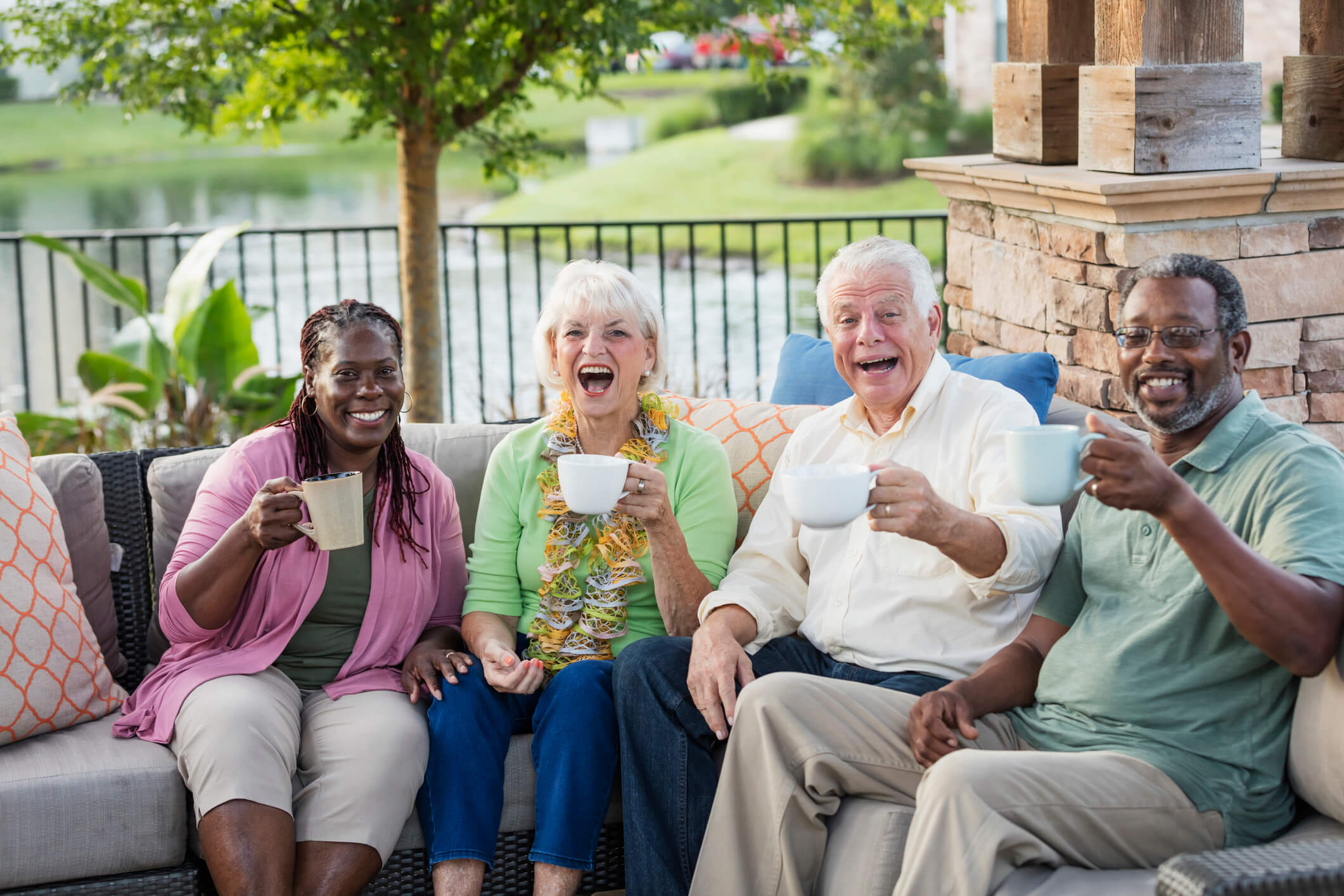 A group of happy elder men and women sitting on a couch in the outdoors having a drink in a cup