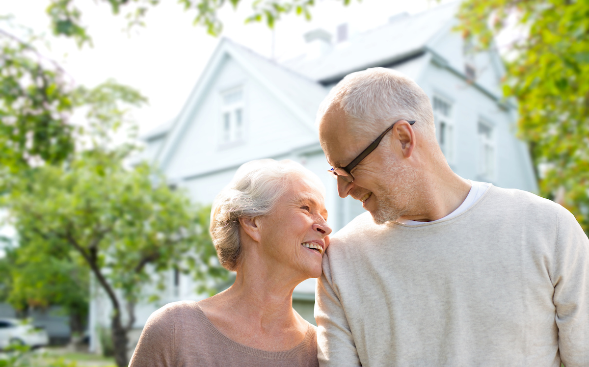 An older couple embracing in front of their new home.