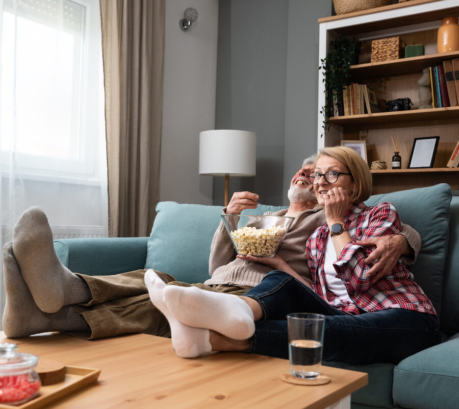 Old retired age couple watching TV at home, old mature couple cheering sport games competition together with laugh smile victory on sofa couch at living room home.