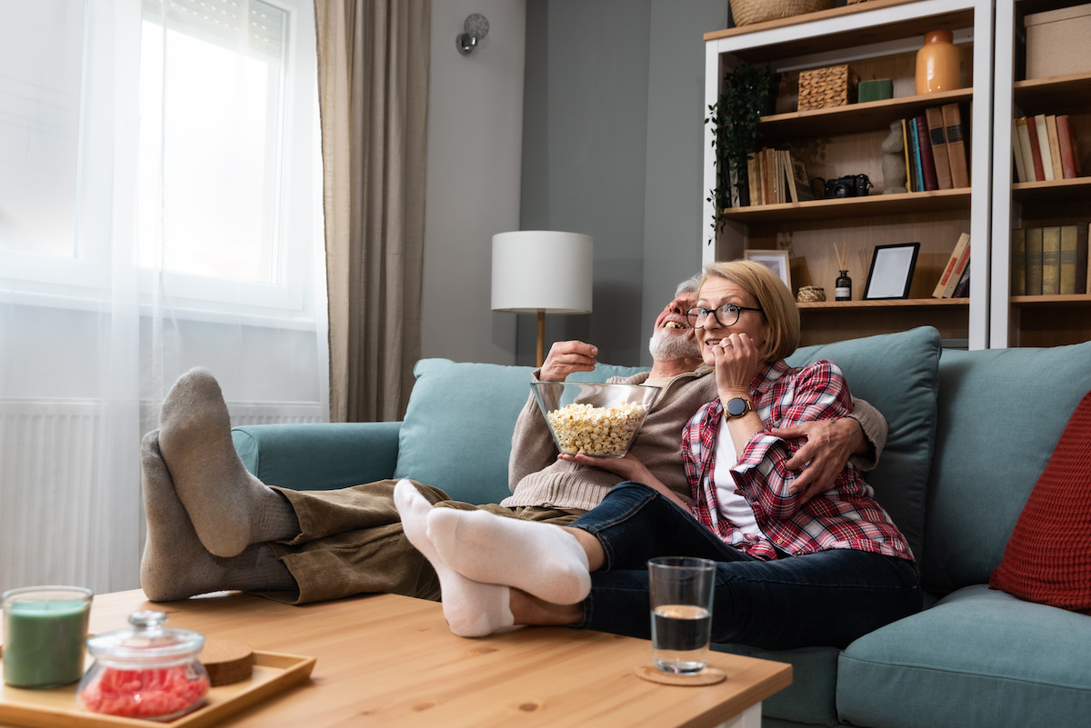 Old retired age couple watching TV at home, old mature couple cheering sport games competition together with laugh smile victory on sofa couch at living room home.