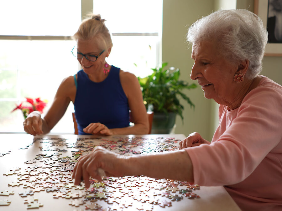 A smiling older woman working on a puzzle with her middle-aged daughter.