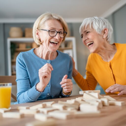 Two older women laughing while playing Jenga.