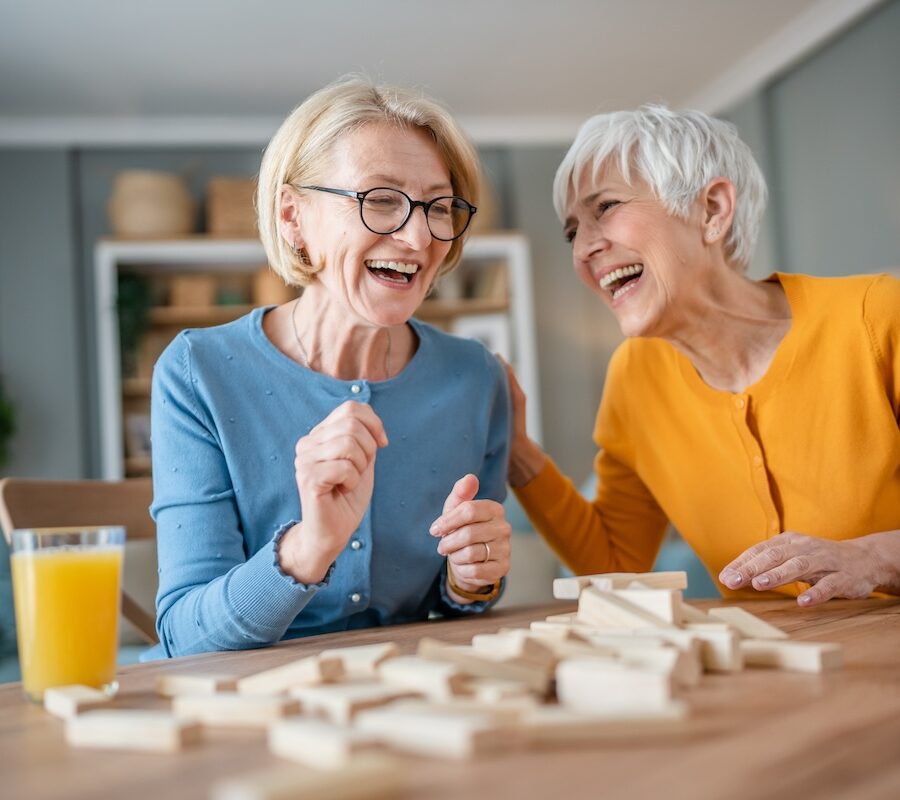 Two older women laughing while playing Jenga.