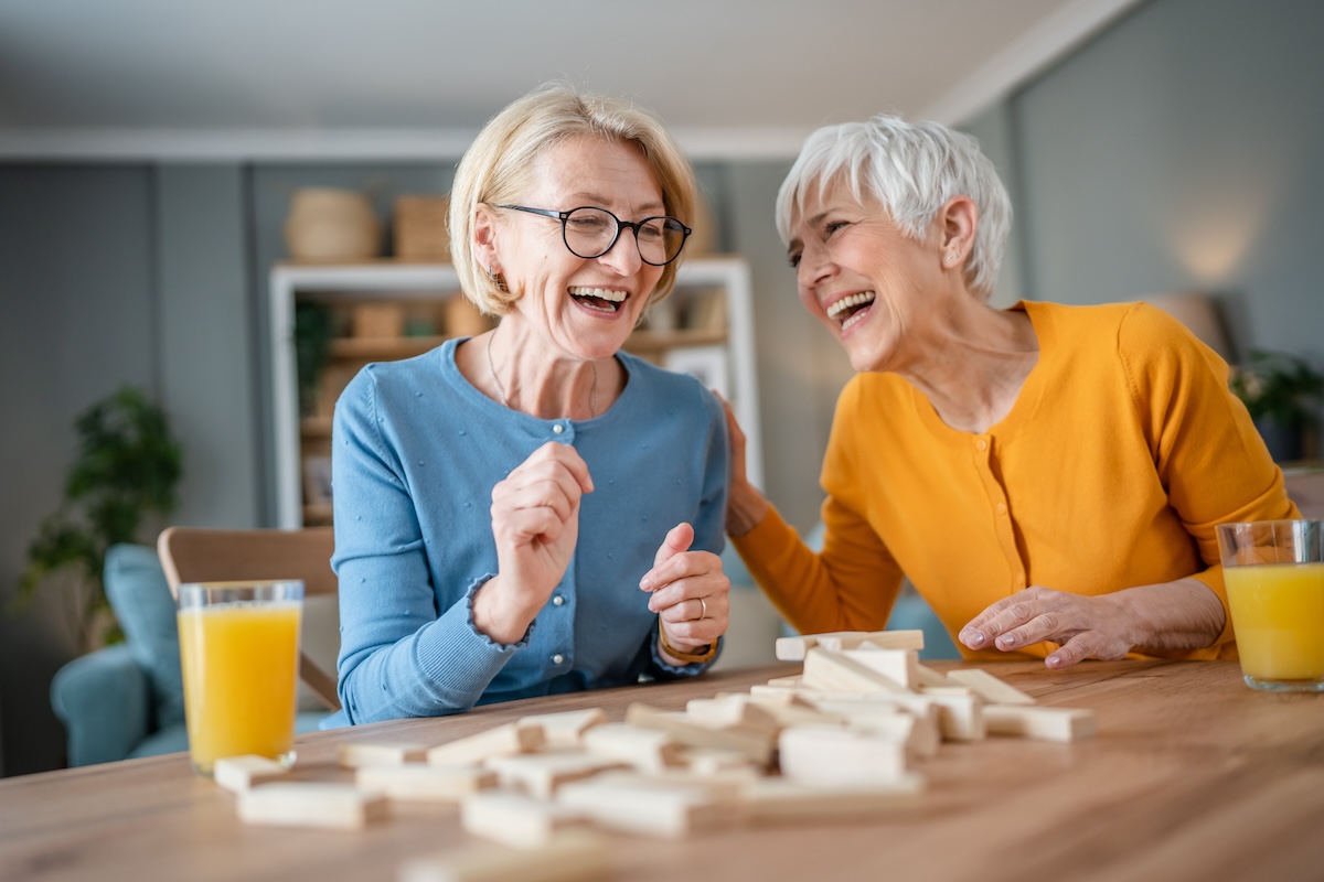 Two older women laughing while playing Jenga.