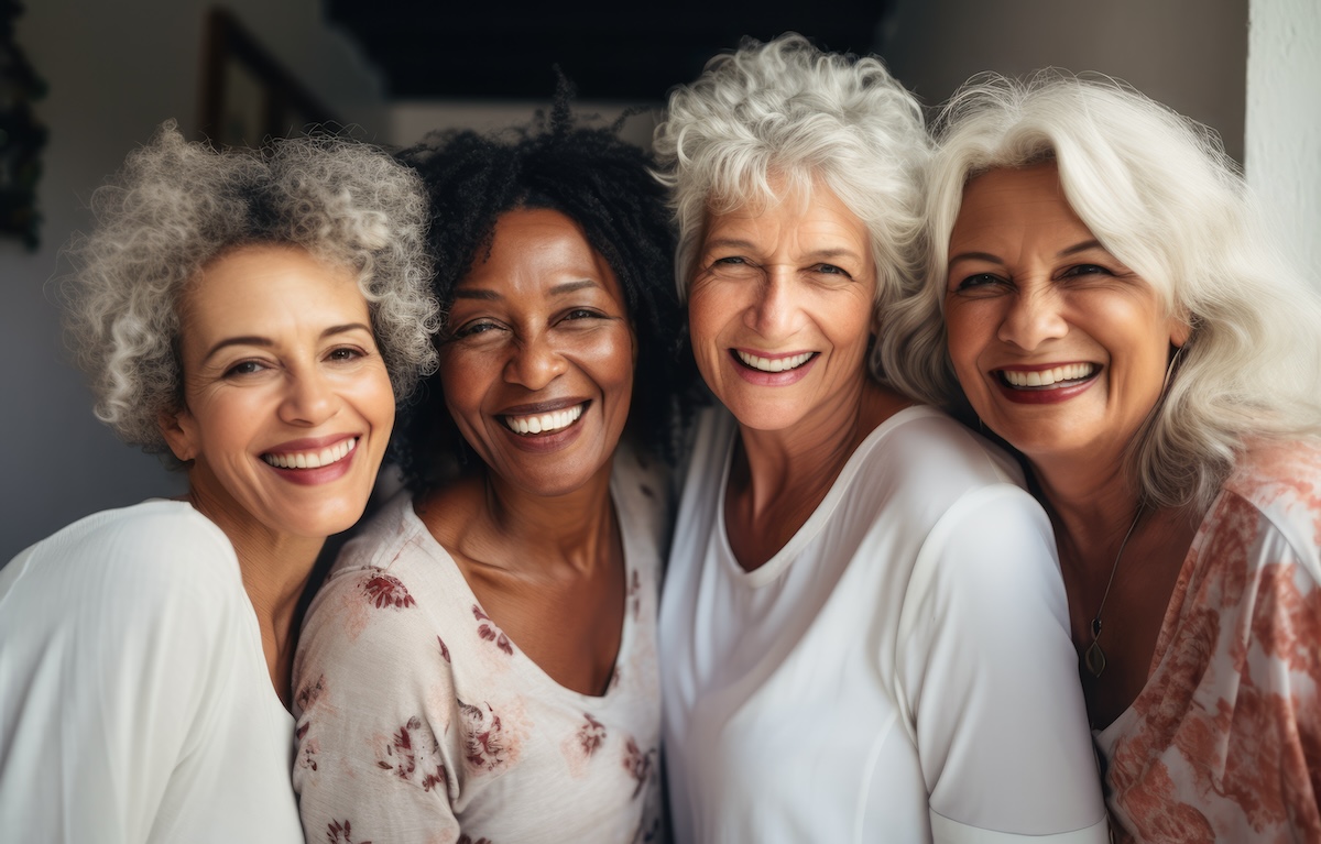 Four joyful senior women together posing for the camera in white clothing.