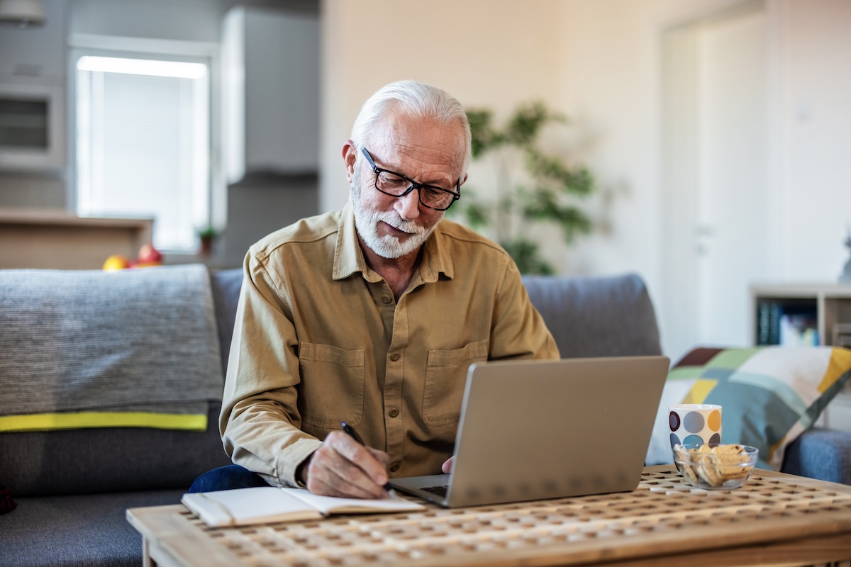 A senior man sits at a desk working on his laptop