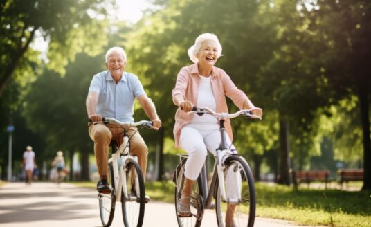 A smiling, active senior couple riding bikes in a vibrant park.