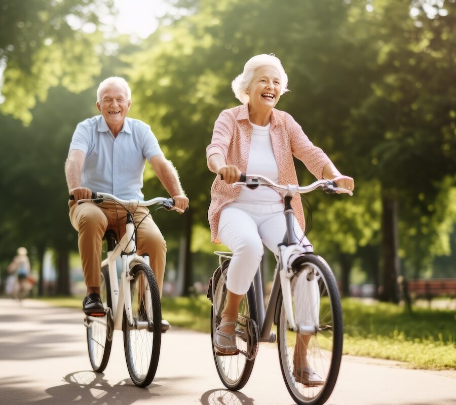 A smiling, active senior couple riding bikes in a vibrant park.