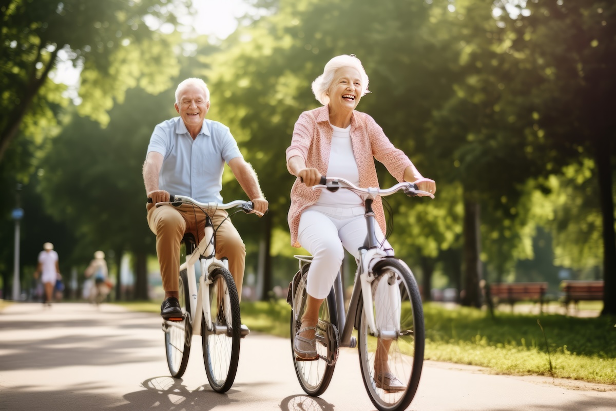 A smiling, active senior couple riding bikes in a vibrant park.