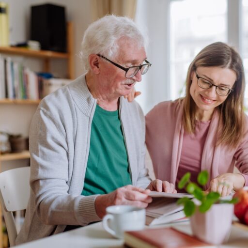 Senior man and his adult daughter sitting at a kitchen table discussing independent senior living communities