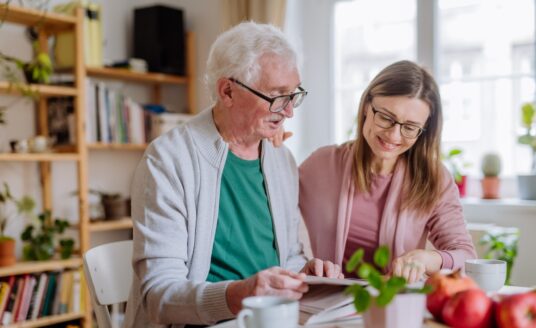 Senior man and his adult daughter sitting at a kitchen table discussing independent senior living communities