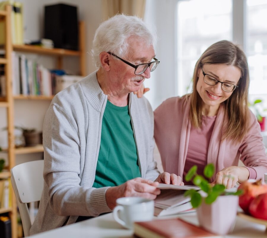 Senior man and his adult daughter sitting at a kitchen table discussing independent senior living communities