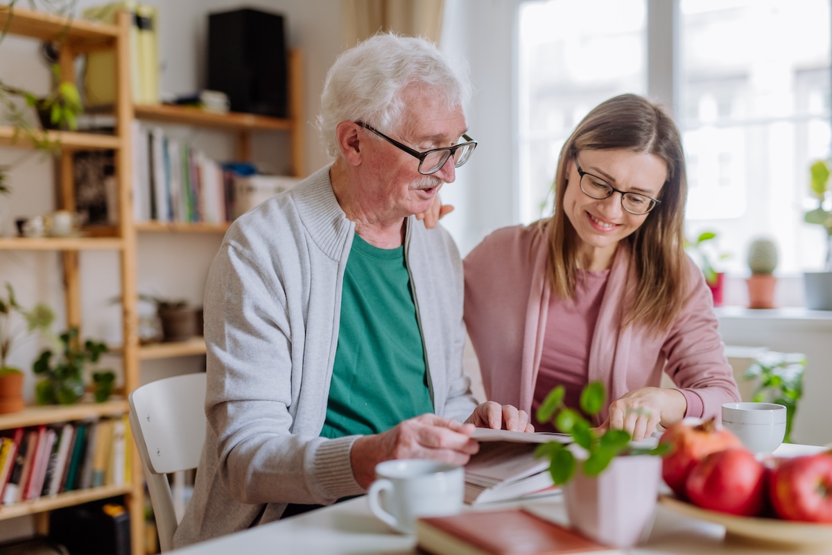 Senior man and his adult daughter sitting at a kitchen table discussing independent senior living communities
