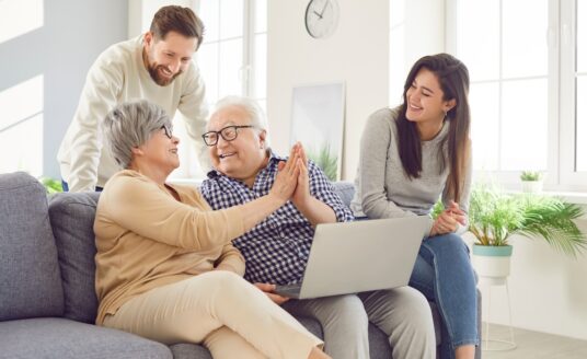 Happy family, aging old parents and adult children, two generations learn using laptop online home.