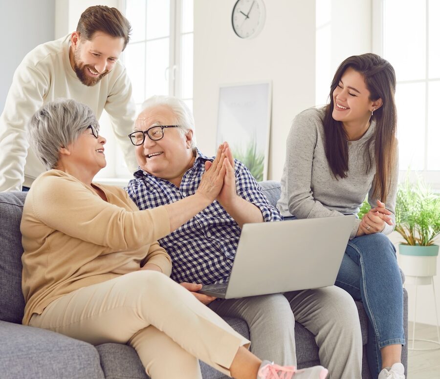 Happy family, aging old parents and adult children, two generations learn using laptop online home.