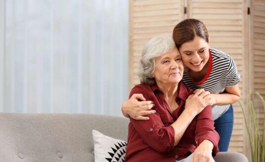 A caregiver embracing an older adult in her home.