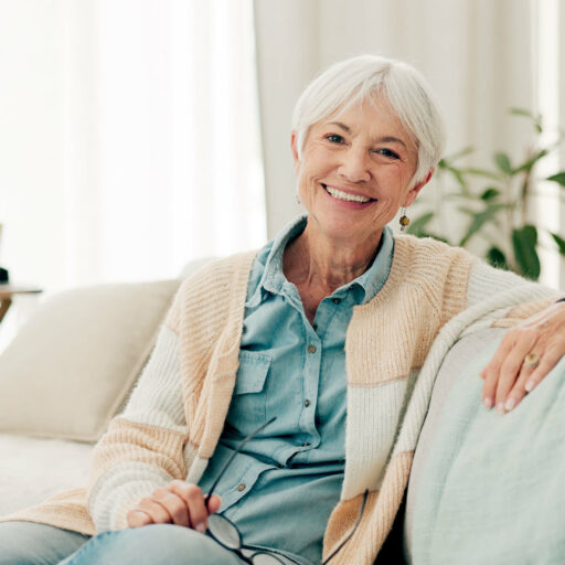 An resident smiling while seated on a sofa in a cozy, well-decorated room.