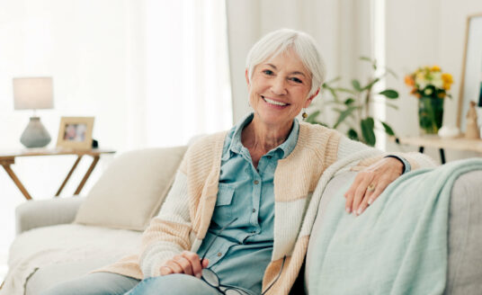 An resident smiling while seated on a sofa in a cozy, well-decorated room.