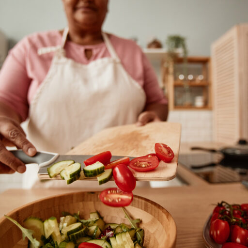 Senior woman putting chopped vegetables into a bowl of healthy foods for seniors