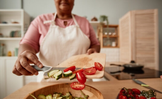 Senior woman putting chopped vegetables into a bowl of healthy foods for seniors
