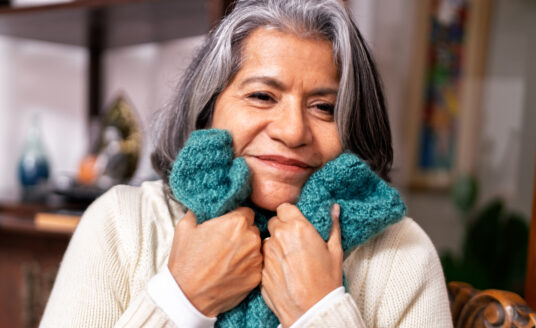Senior woman hugging knitted blanket, one of many comfort items beneficial to dementia patients