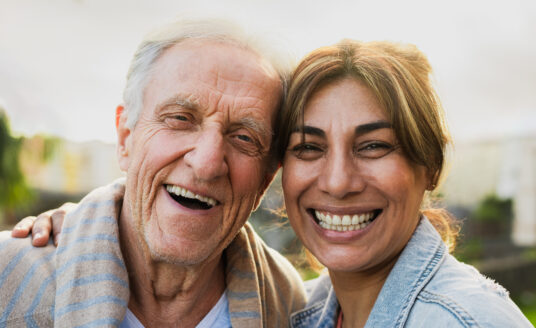 Woman smiling and embracing senior man, maintaining a positive attitude to avoid caregiver burnout.