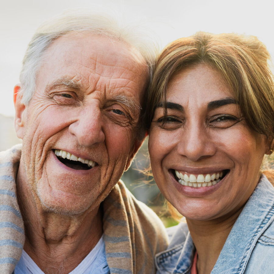 Woman smiling and embracing senior man, maintaining a positive attitude to avoid caregiver burnout.