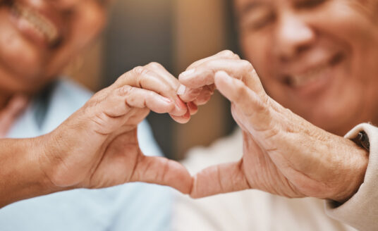 Two seniors making a heart with their hands to support senior heart health