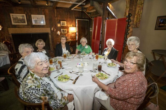 Group of elderly friends dining together around a round table with salads and drinks in a cozy restaurant setting.