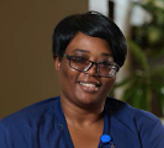 Smiling woman wearing a blue shirt and glasses, indoors.