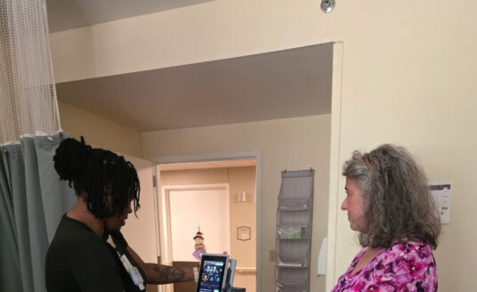 Theresa Wolff watches as staff uses new critical vital sign monitor.