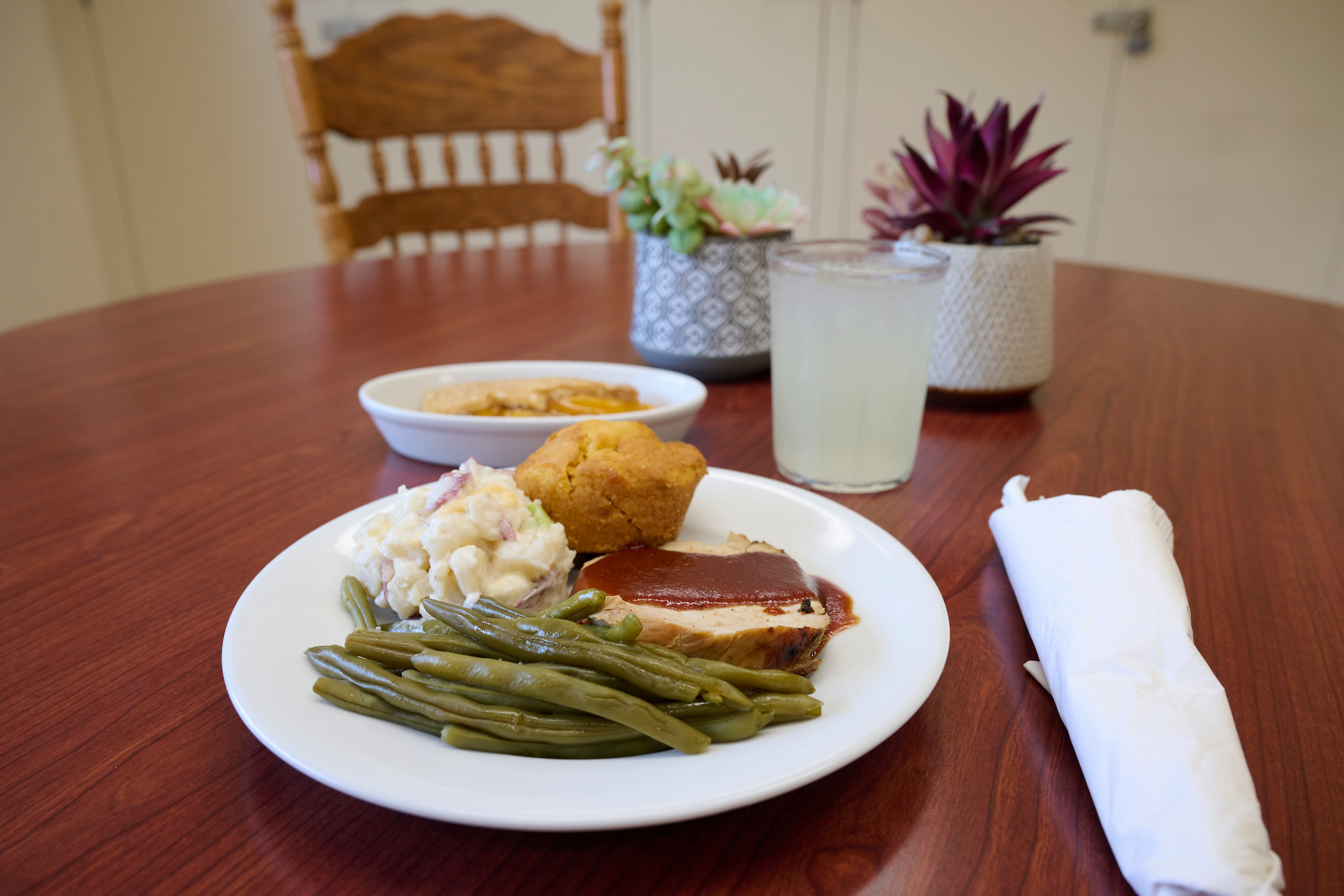 Plate of green beans, sliced meat with sauce, and potato salad on a wooden table.