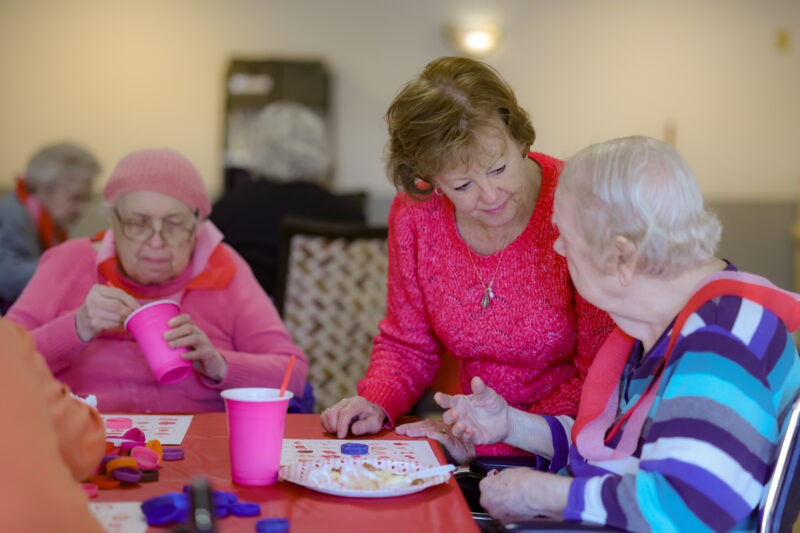 Group of seniors seated around a table, doing crafts with colorful clay and stamps, pink cups nearby.