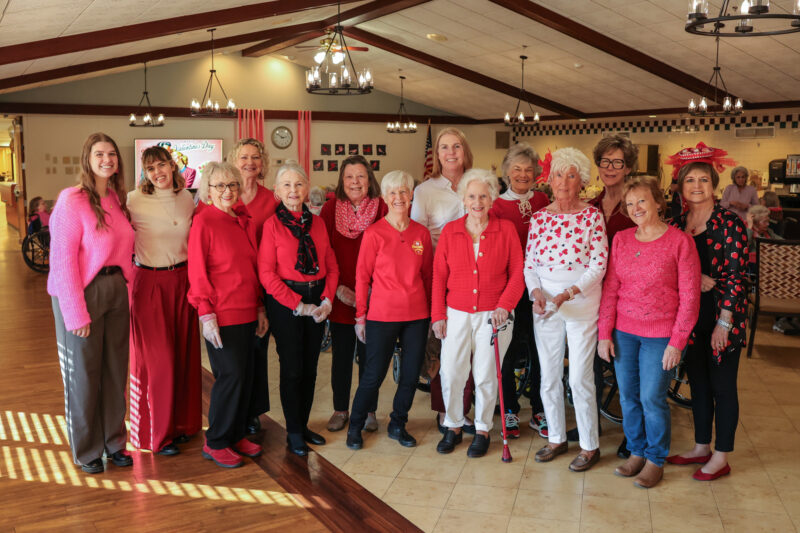 Group of women posing together indoors, many wearing red or pink for a Valentine’s Day event in a community center.