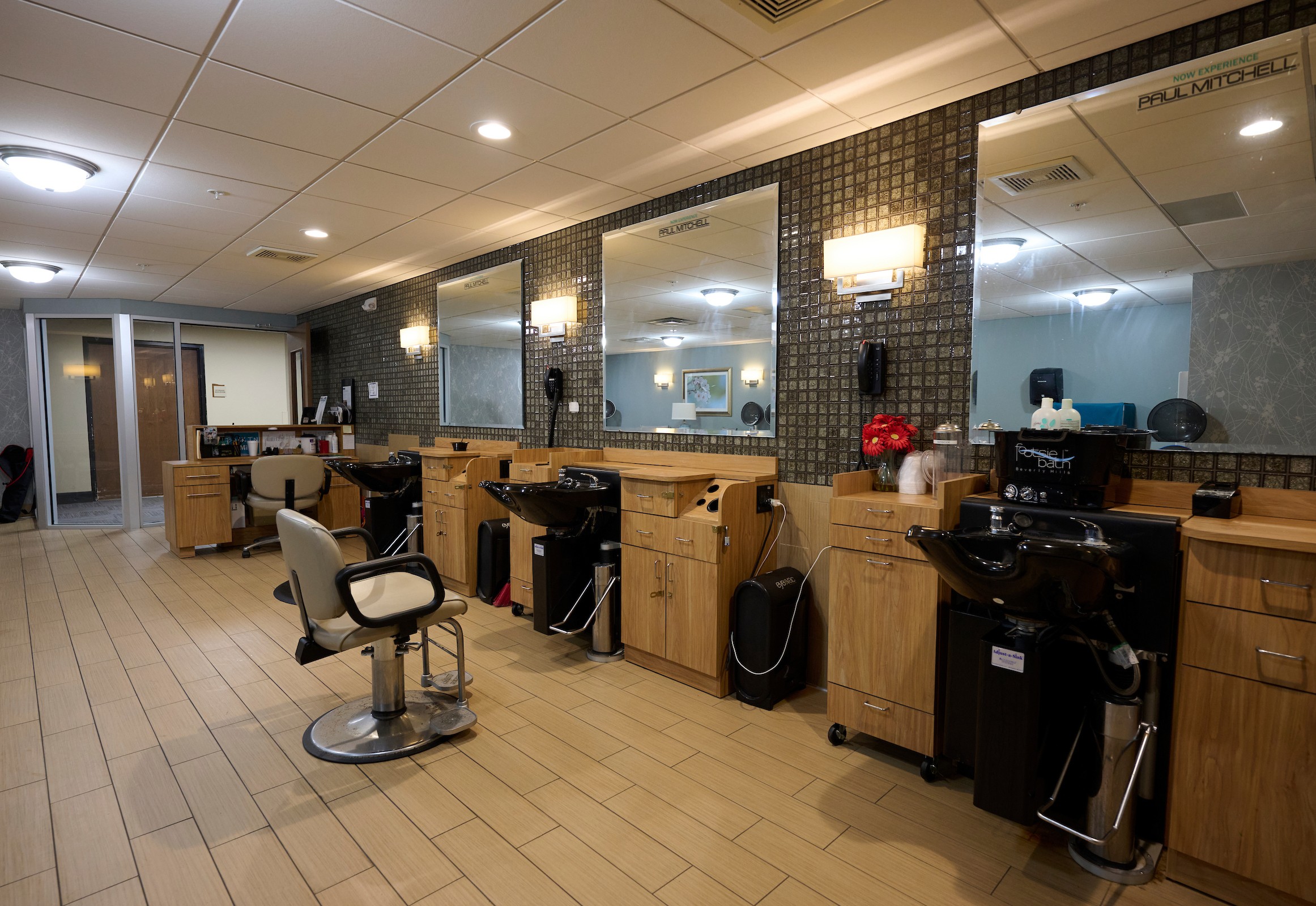 Interior of a hair salon with mirrors, sinks, and wooden cabinets along tiled walls.
