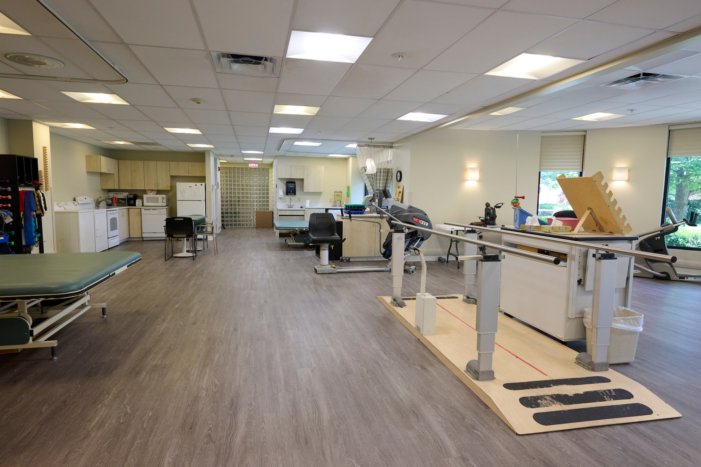 Rehabilitation gym with parallel bars, exercise mats, and medical equipment along the walls.