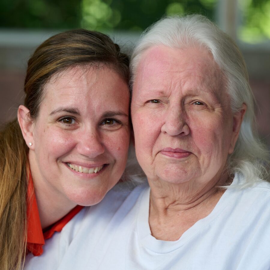 Two women smiling and posing closely together outdoors, showing friendship across generations.