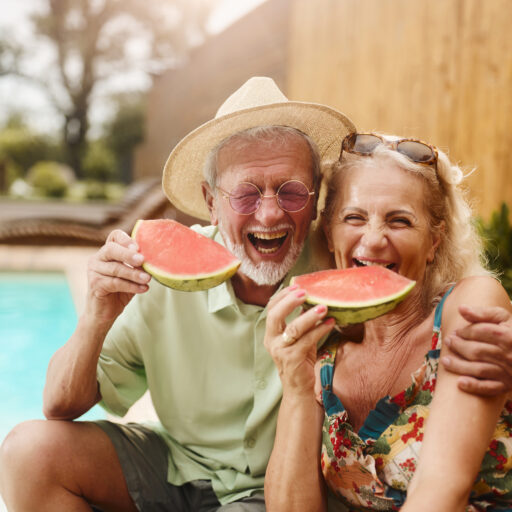 Seniors enjoying a summertime senior bucket list eating watermelon by the pool
