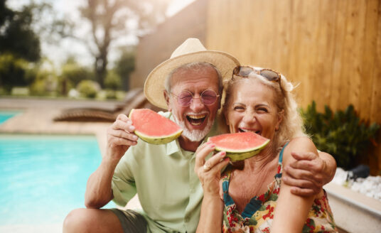 Seniors enjoying a summertime senior bucket list eating watermelon by the pool