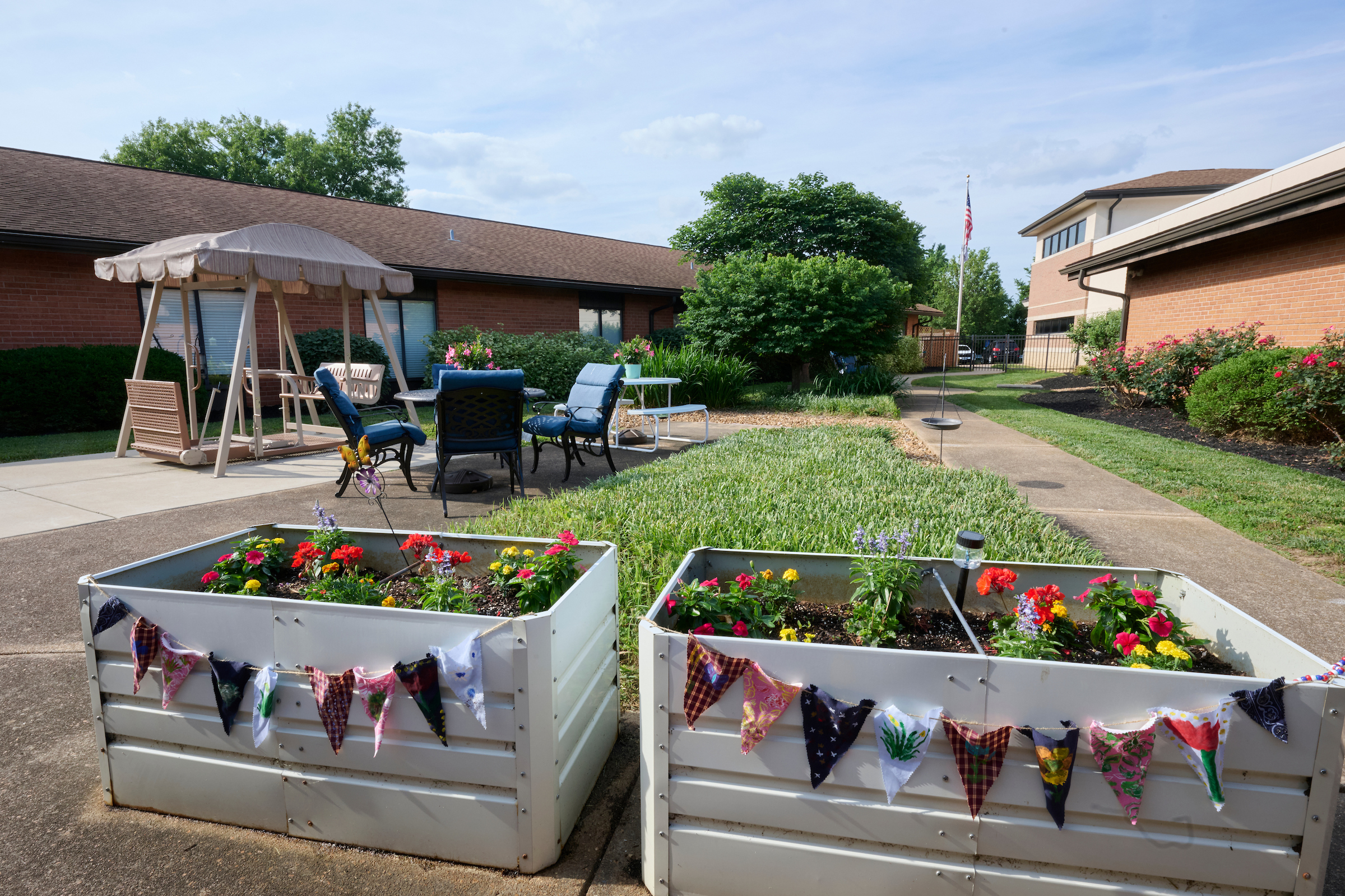 Outdoor courtyard with raised flower planters decorated with bunting, a seating area, and a brick building in the background