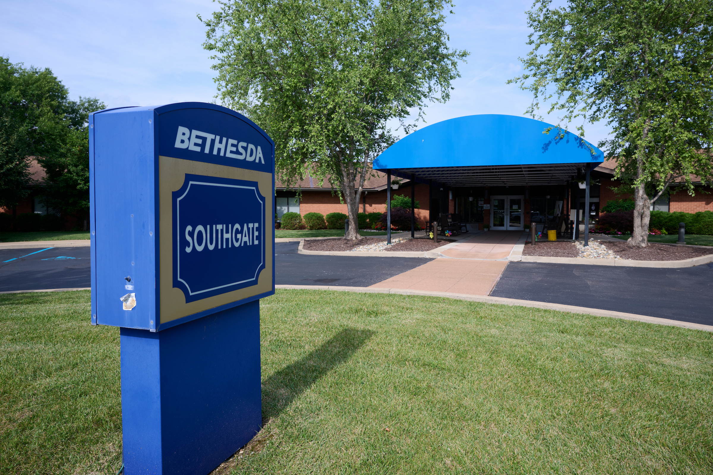 Blue Bethesda Southgate sign on grass near a brick building with a blue curved canopy entrance behind it.