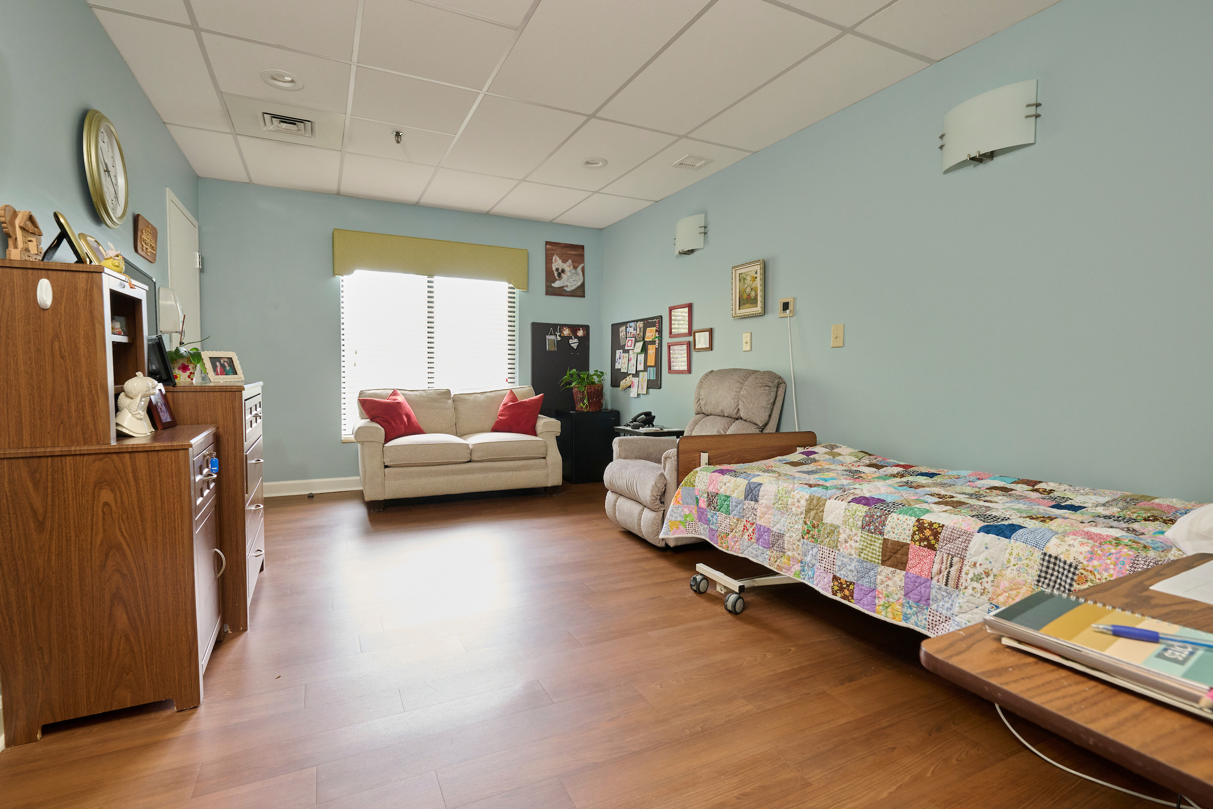 Cozy room with a patchwork quilt bed on the right, a beige sofa in the center, and wooden cabinets along the left wall.