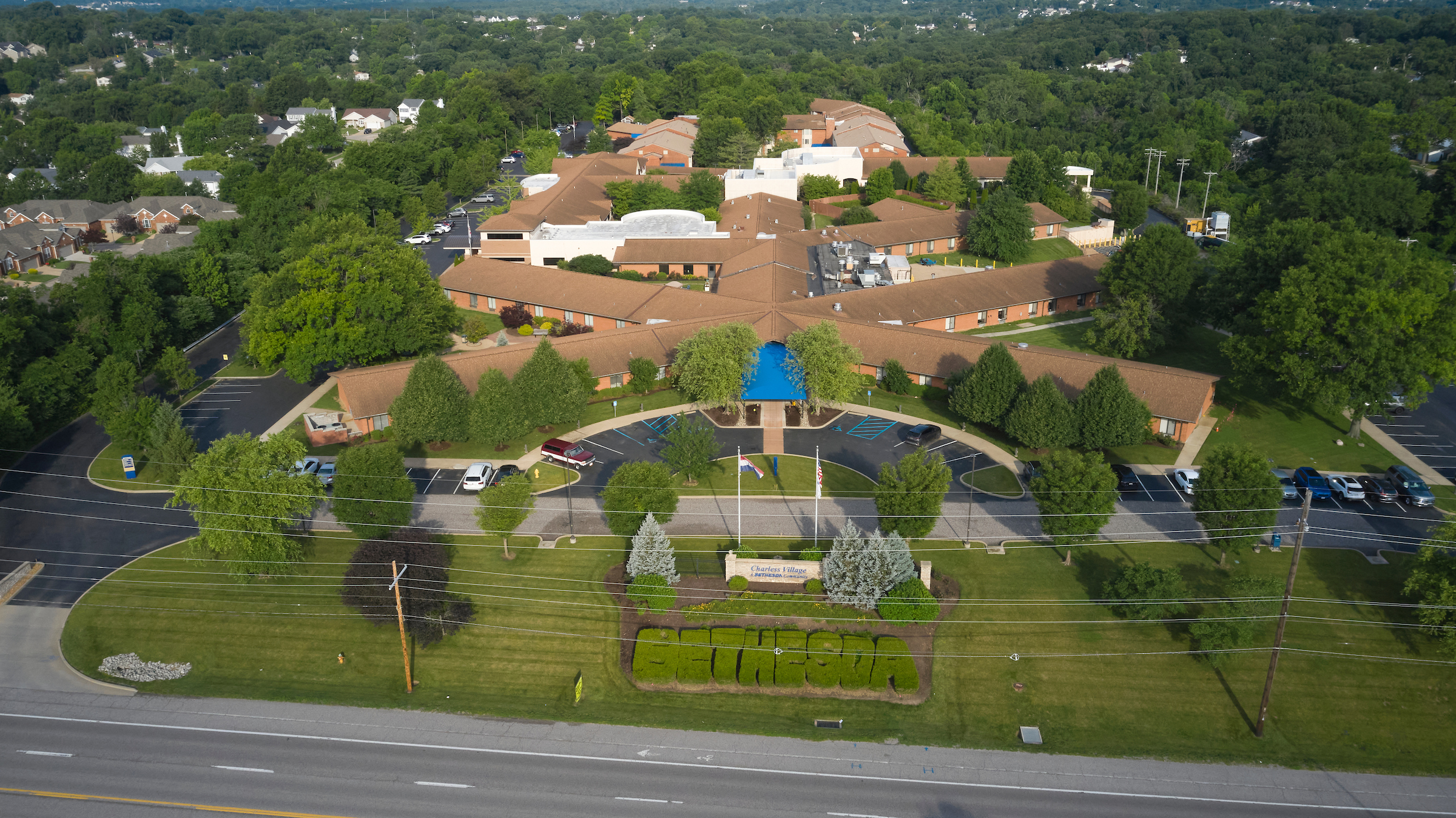 Aerial view of a large brick campus with a central blue entrance canopy, circular driveway, and surrounding green landscaping.